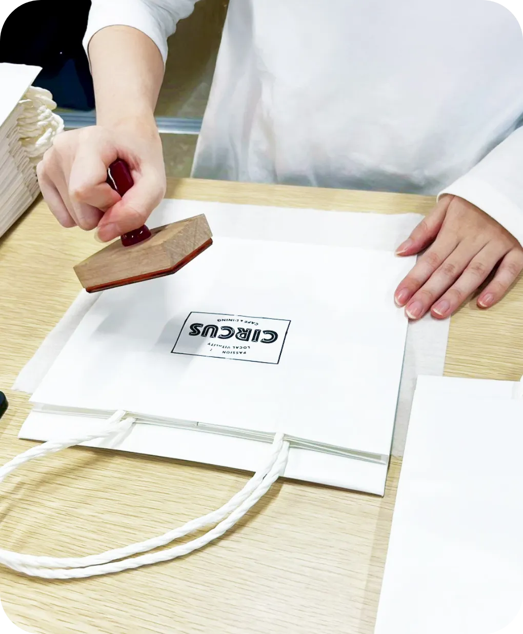 白い紙袋の中央に、ロゴマークのスタンプをまっすぐ押す様子