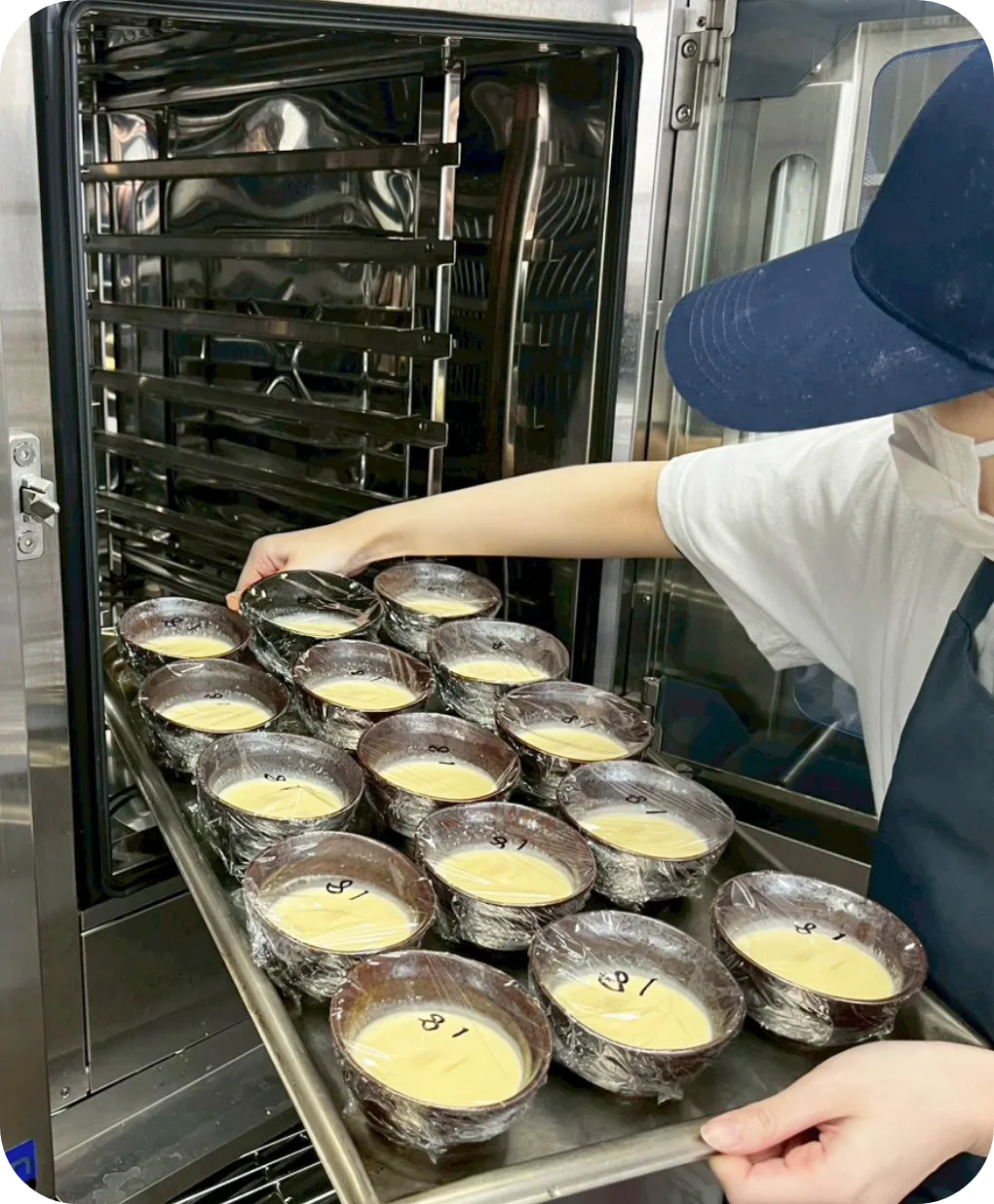 小さな容器を並べたトレイを、業務用オーブンに入れる様子
